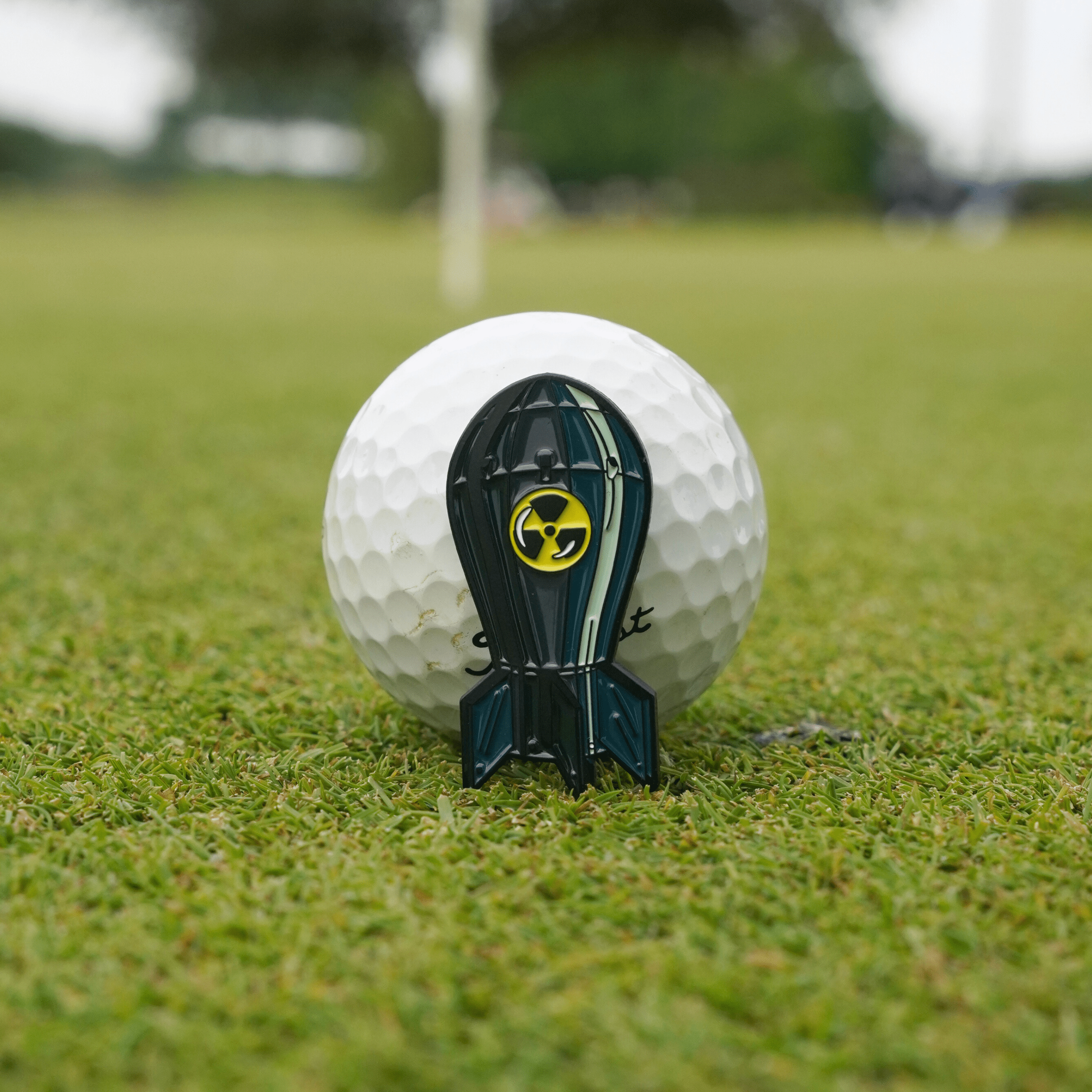 Bombs Away Ball Marker on the green in front of a golf ball, highlighting its compact design and premium finish.